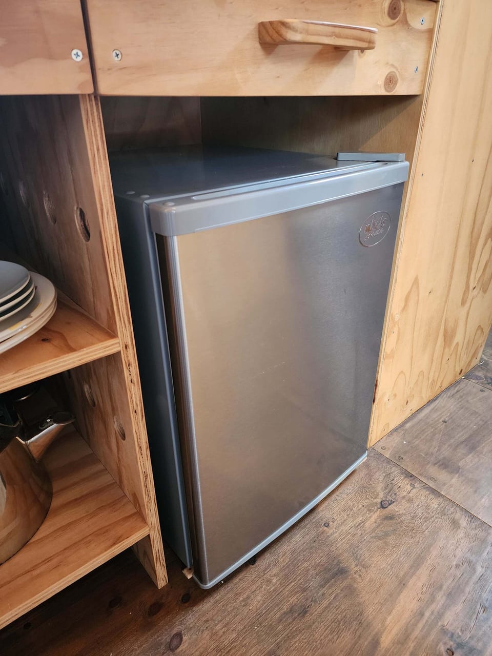 Compact mini fridge tucked into wood cabinetry for easy snack storage.