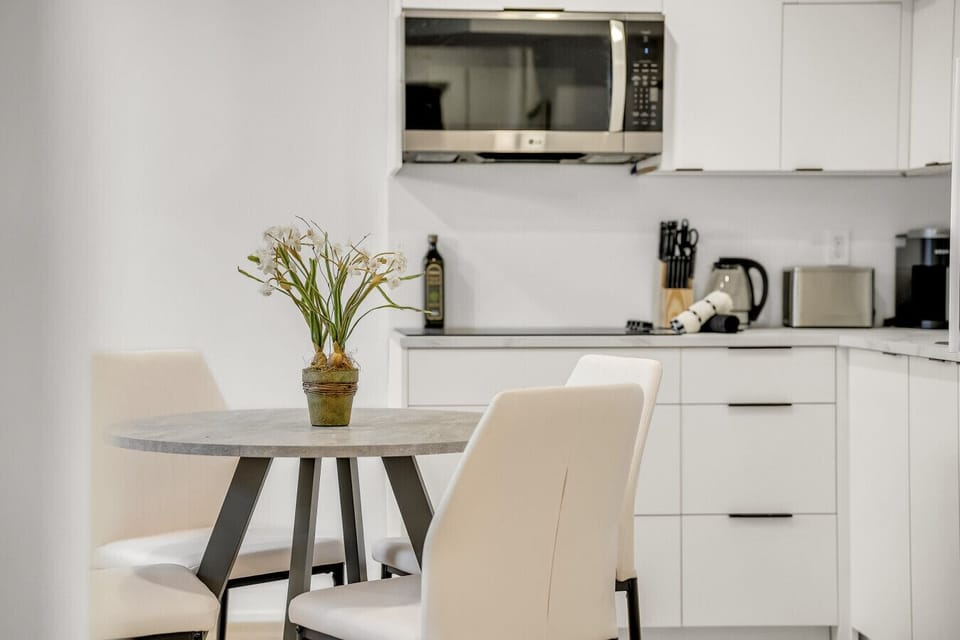 Sleek, fully stocked kitchen and chic dining area. Enjoy a home-cooked meal at the modern table set for four, surrounded by clean white cabinetry and appliances.