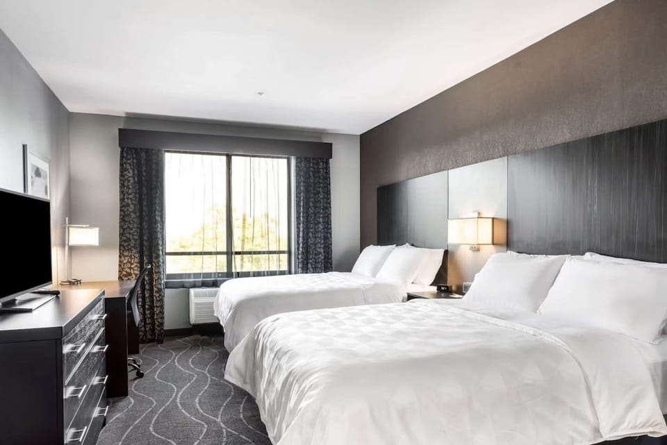 Two queen beds with soft lighting and a view through tall windows