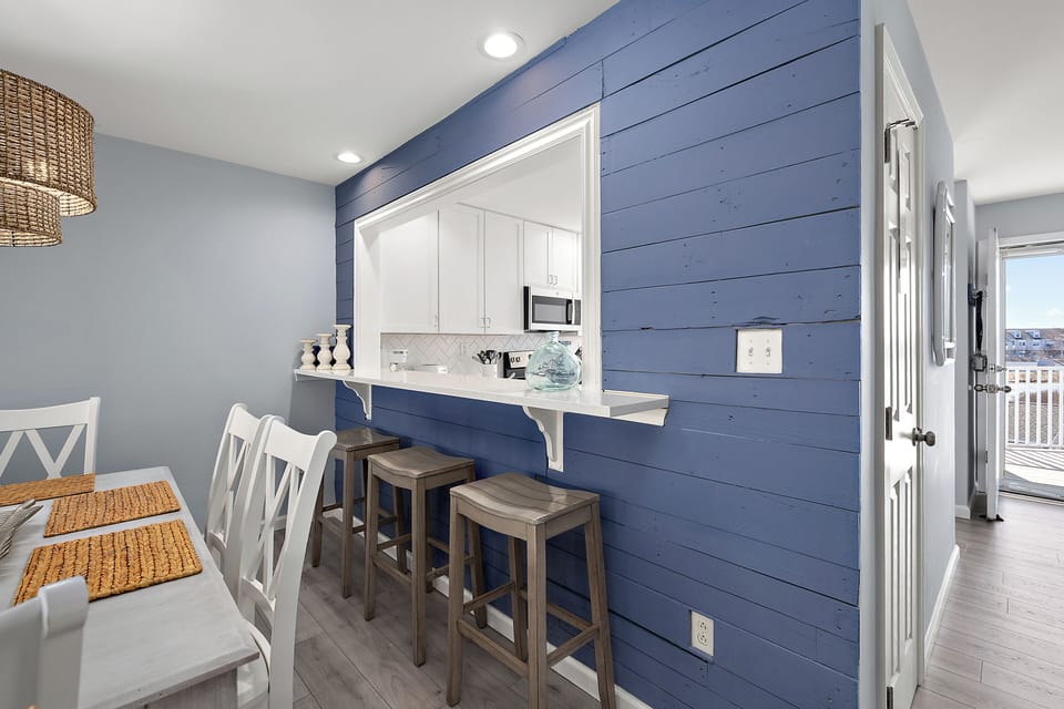 4306 Pettinaro Drive, Bethany Bay - Ocean View - bar - Perspective of the modern kitchen featuring white cabinetry and stainless steel appliances, highlighting a blue shiplap accent wall with a passthrough breakfast bar and stool seating.