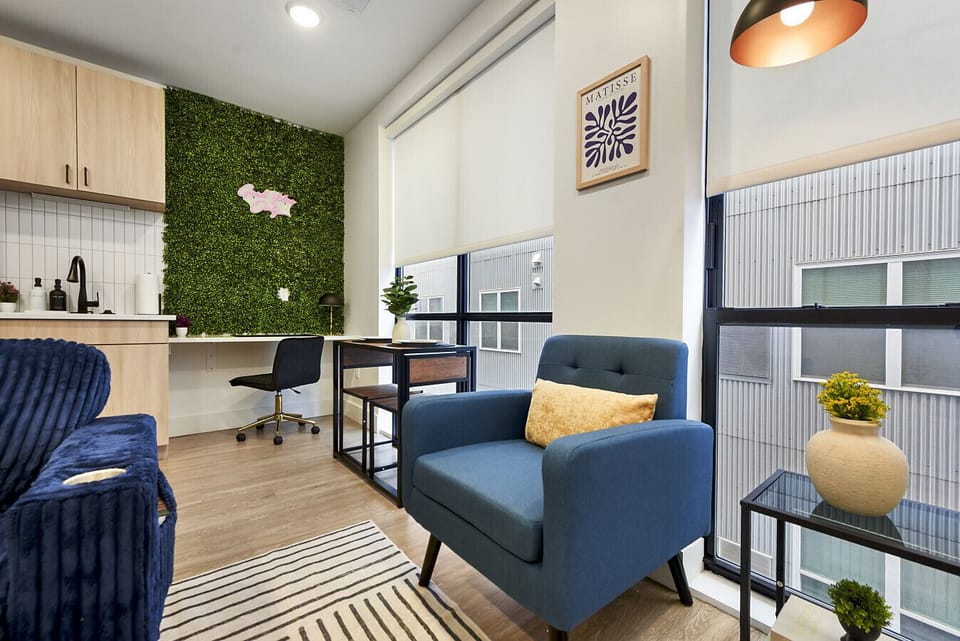 Stylish open-concept space with a cozy blue armchair, dedicated workspace, and vibrant green living wall – ideal for productive and comfortable stays