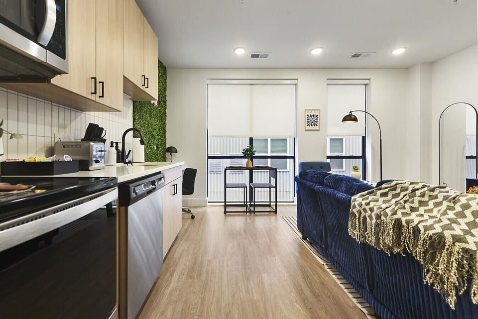 Spacious modern 1 bedroom apartment with full kitchen, plush navy corduroy sofa, smart TV, luxurious green velvet king bed with mustard throw, and large windows —ideal for couples or solo travelers.
