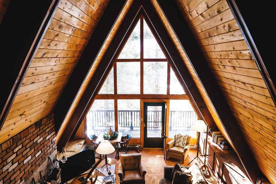Cozy A-frame living room with wood beams and floor-to-ceiling view windows