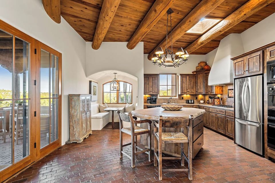 Your rustic kitchen features exposed wooden beams, a large island, and French doors opening to outdoor dining spaces.