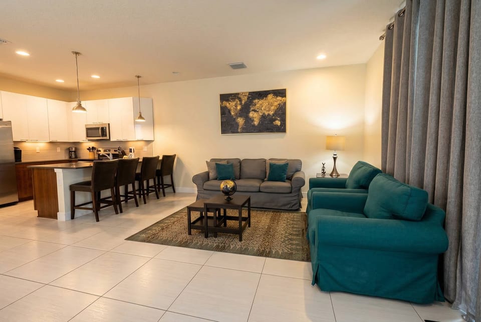 This bright and airy living area invites you to relax with a plush gray sofa and vibrant teal chairs, while the decorative world map adds a sense of wanderlust, making it the perfect spot to unwind after your adventures.