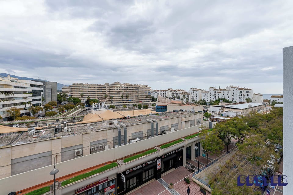 Urban cityscape with shops, tree-lined walkway, and residential buildings with balconies. A mix of styles and clean design captures the rhythm of modern city life.