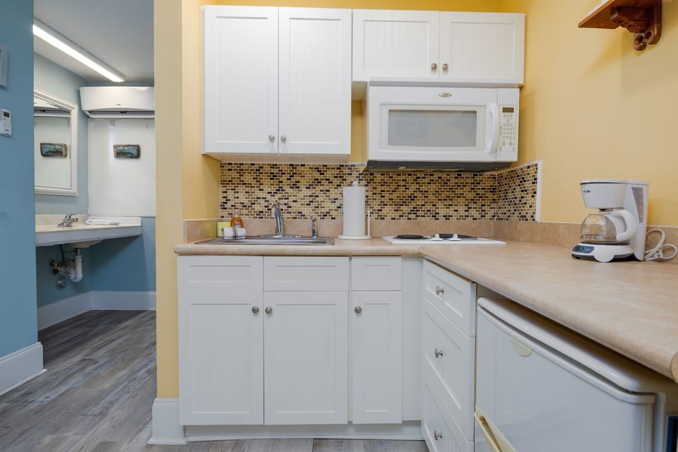 Compact kitchenette with white cabinetry, microwave, mini fridge, and coffee maker—perfect for quick meals and easy mornings