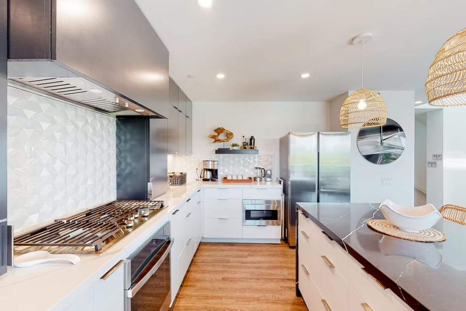 Cook and entertain in this fully equipped, modern kitchen featuring sleek appliances, ample counter space, and a stylish coffee station. Perfect for preparing meals or enjoying a cozy breakfast during your Oceanside getaway.
