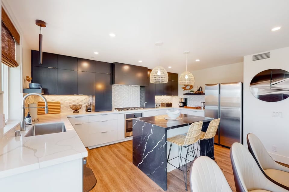 Cook and entertain in this fully equipped, modern kitchen featuring sleek appliances, ample counter space, and a stylish coffee station. Perfect for preparing meals or enjoying a cozy breakfast during your Oceanside getaway.
