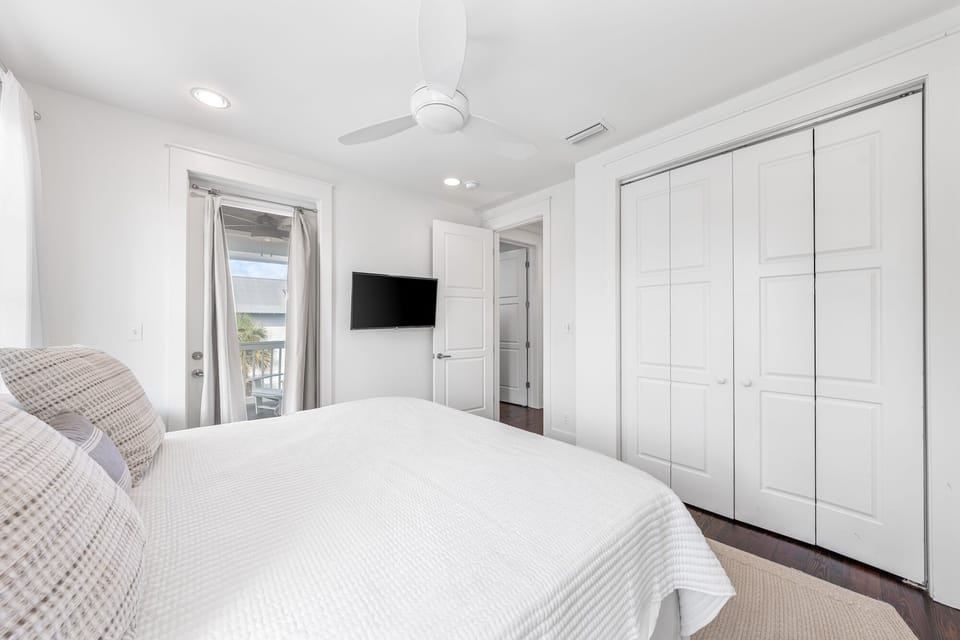 Your bright bedroom features a plush bed, mounted TV, and spacious wardrobe, with private balcony access for fresh sea breezes.