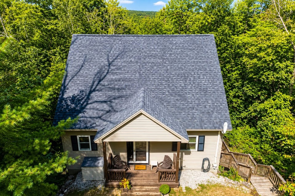 Aerial cottage view tucked in woods near lakes, trails, village, and swimming