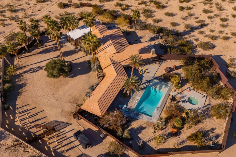 A private desert oasis featuring a sparkling pool, spa, and expansive grounds surrounded by towering palms.