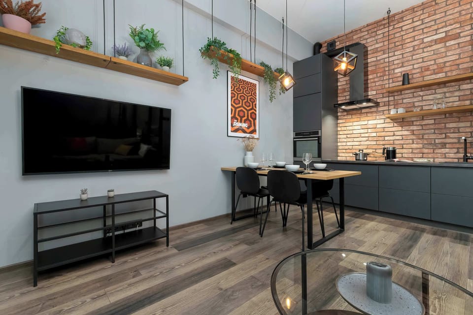 A living and dining area with a wall-mounted TV and an open kitchen in the background. The layout is practical and well-organized.