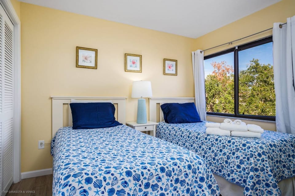 Unwind in your bright twin bedroom with cheerful blue bedding and peaceful garden views streaming through large windows.