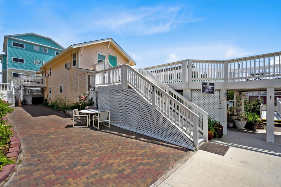 Charming beach house with elevated deck and parking area beneath in a coastal residential setting.