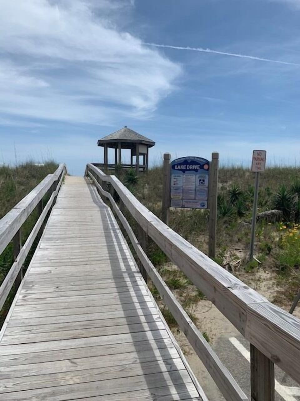 Wooden boardwalk leads to a charming lakeside gazebo, perfect for peaceful moments surrounded by natural dunes and native vegetation.