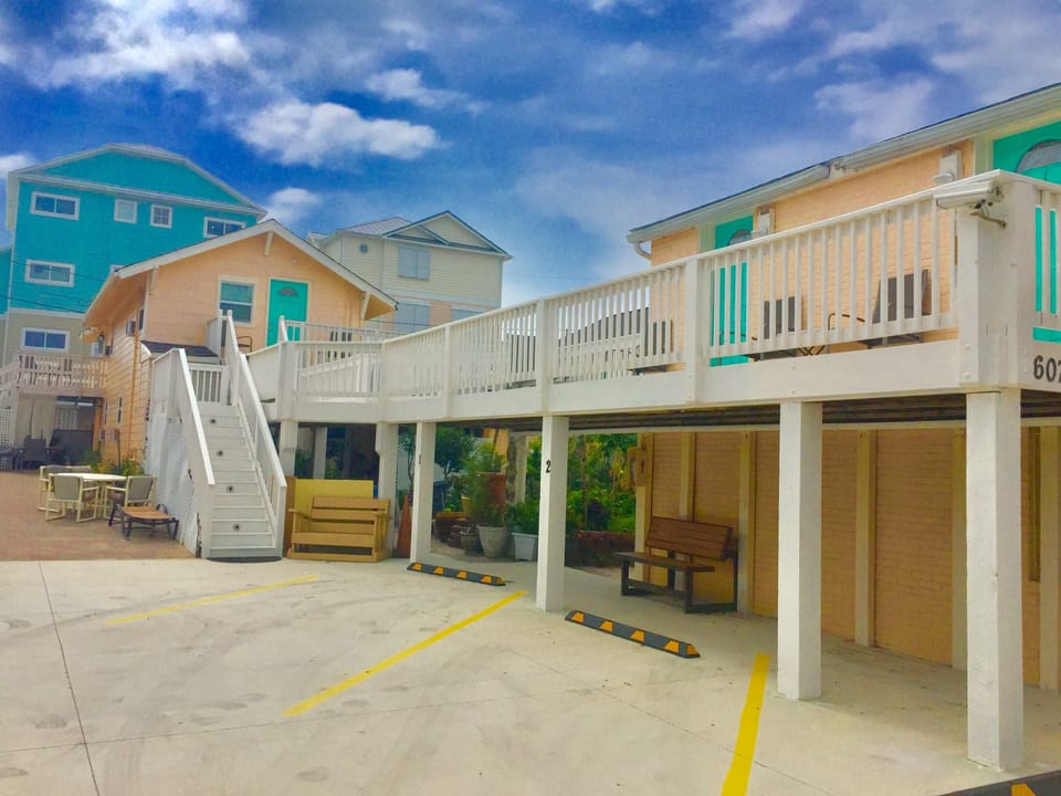 Beachside property with covered parking and elevated deck overlooking colorful coastal homes under blue skies.
