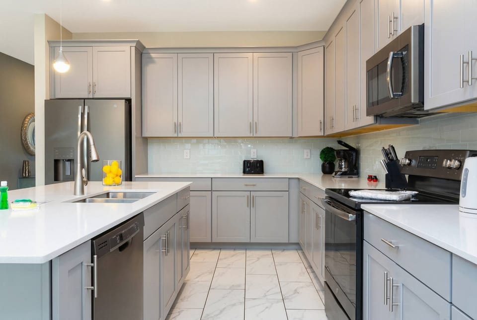 Cook with ease in a bright modern kitchen with gray cabinetry, stainless steel appliances, white countertops, a large island, pendant lighting, and clean neutral finishes.