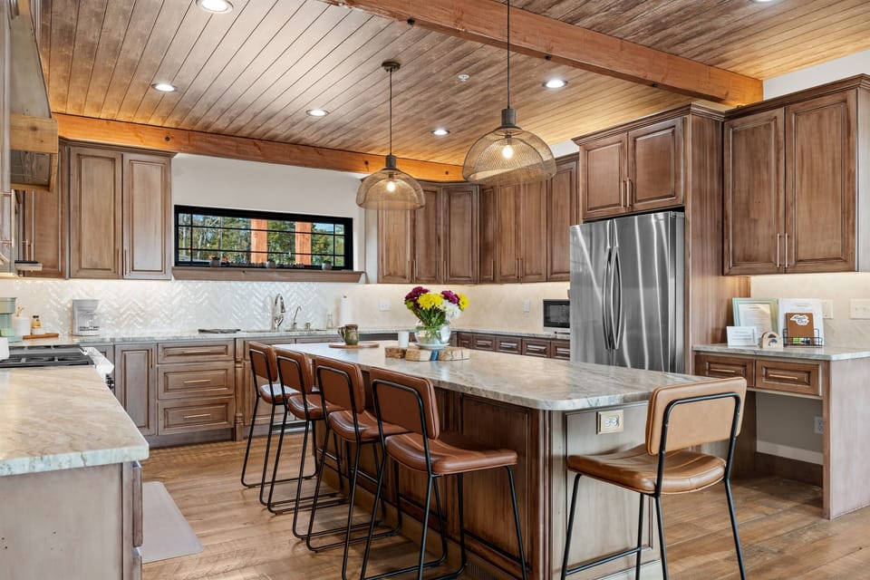 Warm wood tones, soft lighting, and comfy island seating make this kitchen feel instantly cozy. It’s the kind of space where coffee lingers in the morning, meals are made together, and conversations naturally carry on.