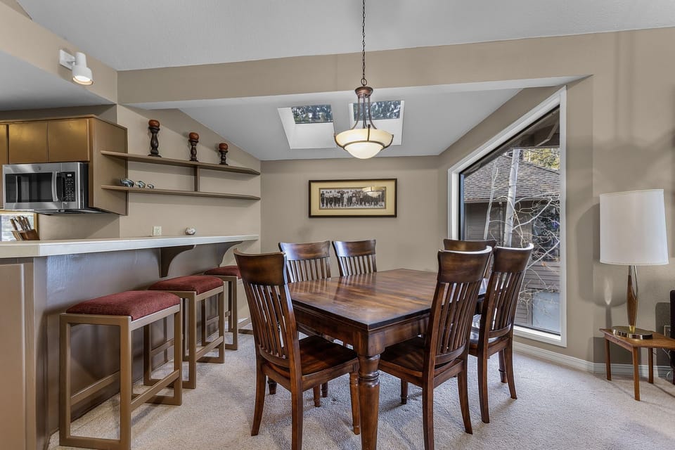 Gather around your elegant dining table where warm wood tones and natural skylight create the perfect setting for memorable meals together.