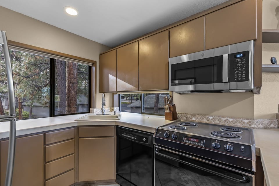 Your fully equipped kitchen awaits with stainless steel appliances, ample counter space, and peaceful views of mature trees through the window.