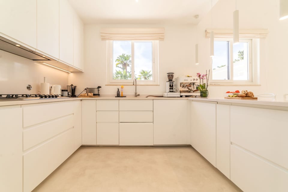 Modern white kitchen with central island and palm tree views — Villa Aroeira I, holiday villa in Herdade de Aroeira