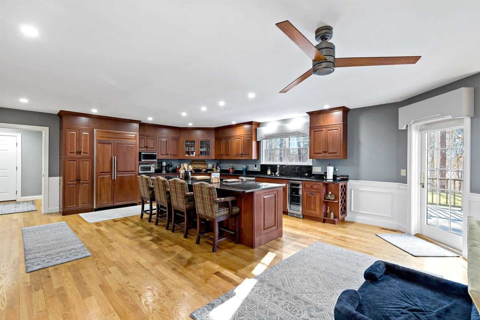 Spacious Cape Cod kitchen with granite countertops, island seating, stainless appliances, and deck access, built for easy family meals.