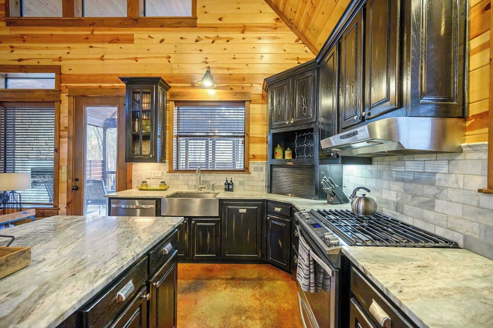 Bright cabin kitchen with marble counters, farmhouse sink, and black cabinets.