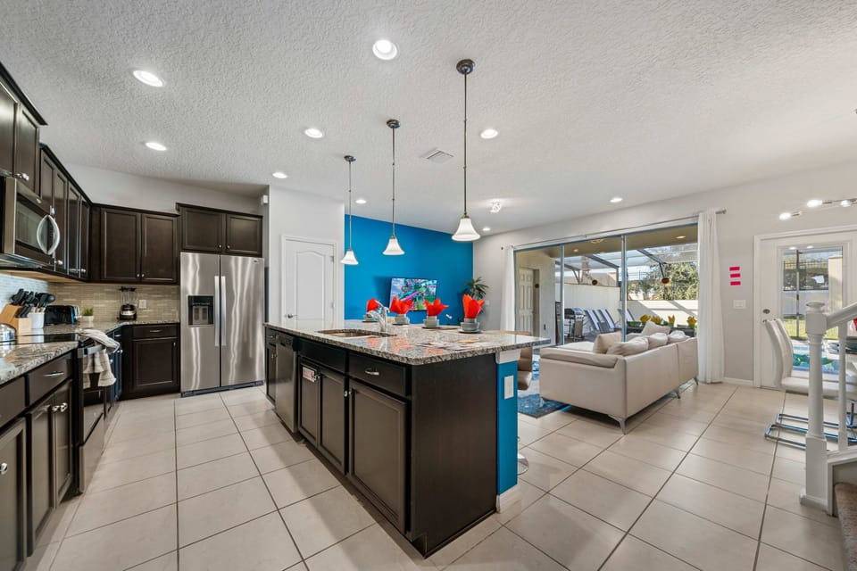Open-concept hub with granite island seating, pendant lighting, and a bold blue accent wall-cook, lounge, and slide open the doors to your screened pool patio.