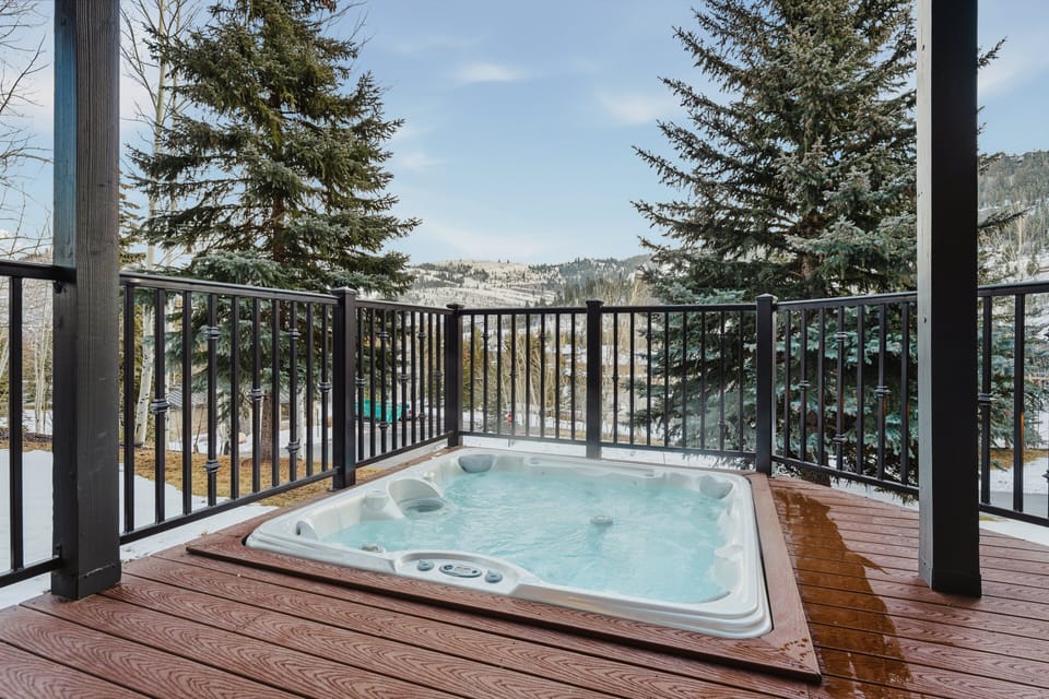 Private outdoor deck featuring a hot tub surrounded by forest views. Accessible from the entertainment room, this space is perfect for unwinding after a day of skiing or mountain adventures.