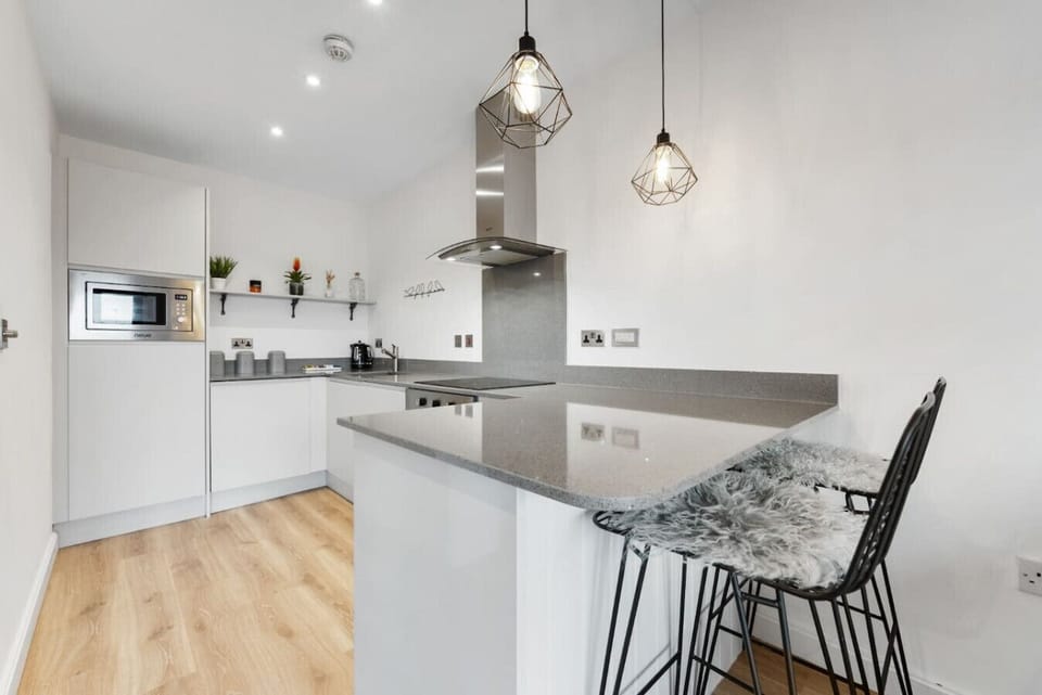 A sleek white kitchen with an island, stools, and built-in appliances.