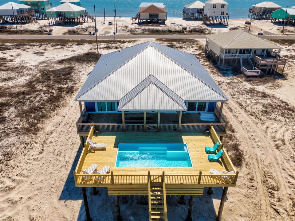 Beachfront home with private pool and deck, surrounded by coastal community and sparkling ocean waters.