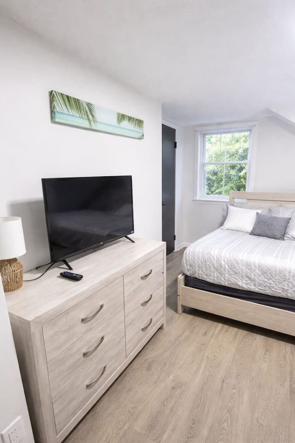 This serene second bedroom offers a comfortable queen-sized bed, a large dresser with a smart TV, and plenty of natural light for a bright and airy feel.