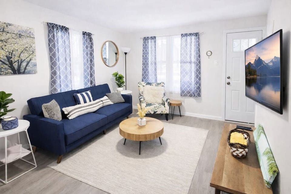 This bright, open-concept living area offers a stylish blue sofa and smart TV, perfectly positioned just steps away from the dining table and fully equipped kitchen.