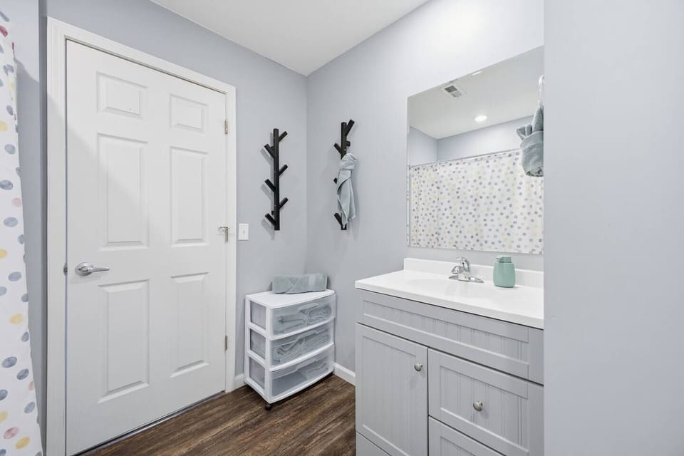 Bright bath with tub/shower, sleek vanity, wood floors, and extra storage.