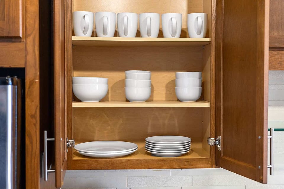 Organized kitchen cabinets displaying neatly arranged dishes, bowls, and glassware. Plenty of storage and essentials provided to make guests feel at home and enjoy a hassle free stay.