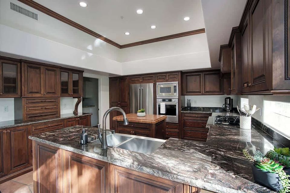 Fully equipped kitchen with stainless steel KitchenAid appliances, dual kitchen sink, a sleek kitchen island, endless counterspace, and cabinets.