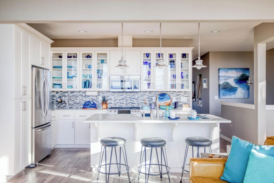 Your bright kitchen awaits with gleaming white cabinets, coastal blue accents, and a spacious island perfect for morning coffee or evening conversations.