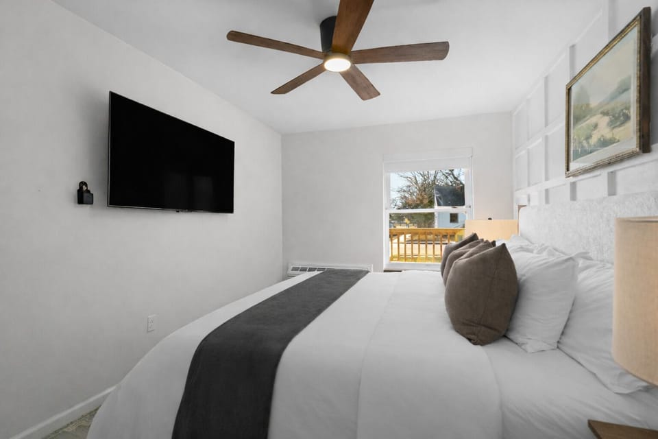 Peaceful bedroom with plush bedding, ceiling fan, and wall-mounted TV—designed for restful nights and a relaxing, comfortable stay.