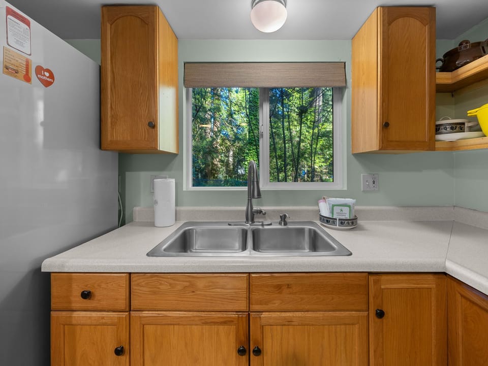 Your fully equipped kitchen overlooks peaceful forest views, perfect for preparing meals while enjoying nature's tranquil backdrop through the window.
