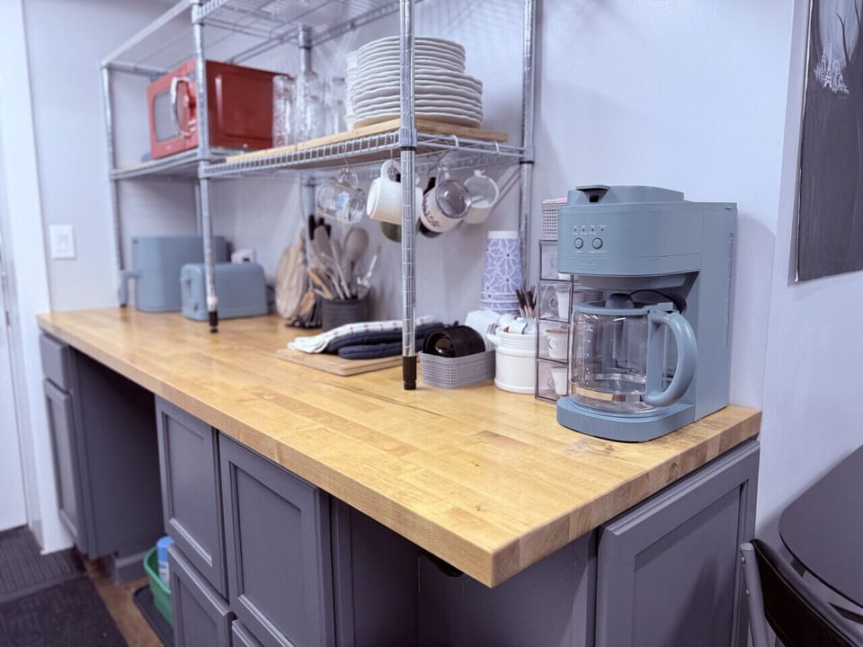 Kitchenette including microwave, airfryer, toaster, slow cooker, knives, flatware, plates, bowls, glasses, mugs, and coffee bar.