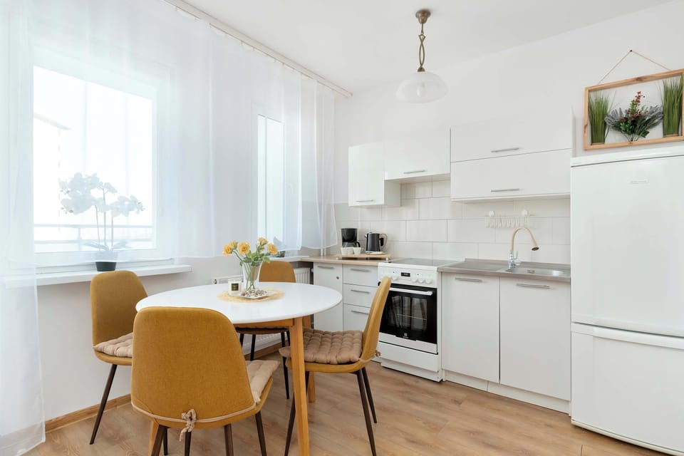 The kitchenette with white cabinets, a round dining table, and mustard-colored chairs. The space is modern, clean, and ready for meal preparation.