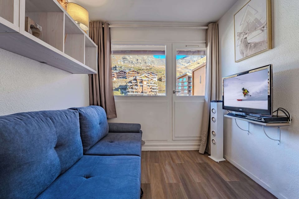 Cozy lounge with smart TV and large window framing Val Thorens chalets — relax after the slopes.