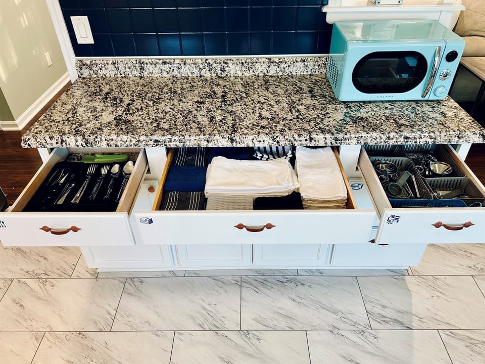 Kitchen drawers organized with a full set of silverware and a variety of kitchen towels, essential cooking tools, including measuring cups, measuring spoons, can opener, vegetable peeler, grater, and other utensils, neatly arranged and easy to access.