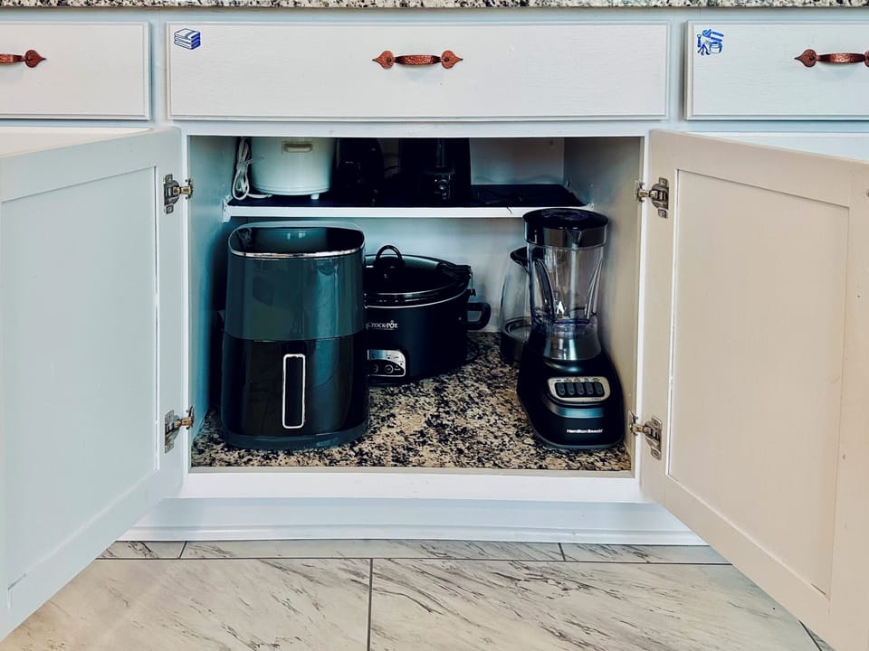 Dedicated kitchen cabinet stocked with small appliances, including an air fryer, large crock pot, small crock pot, hand mixer, toaster, electric kettle, and blender. Fully equipped for everyday cooking and extended stays.