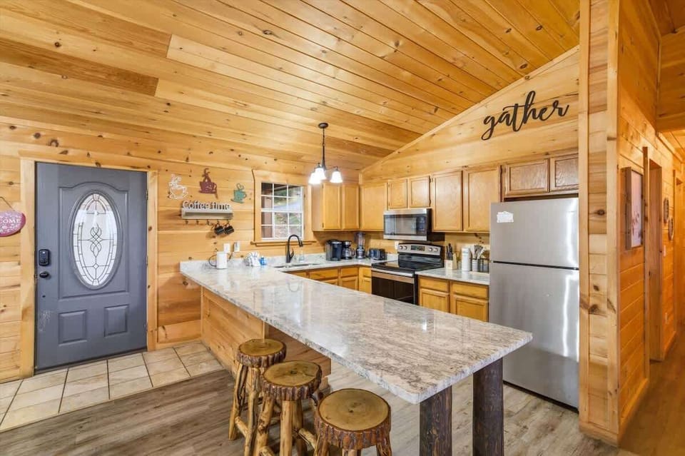 Open-concept kitchen featuring stainless steel appliances, spacious island seating, and warm cabin finishes. 