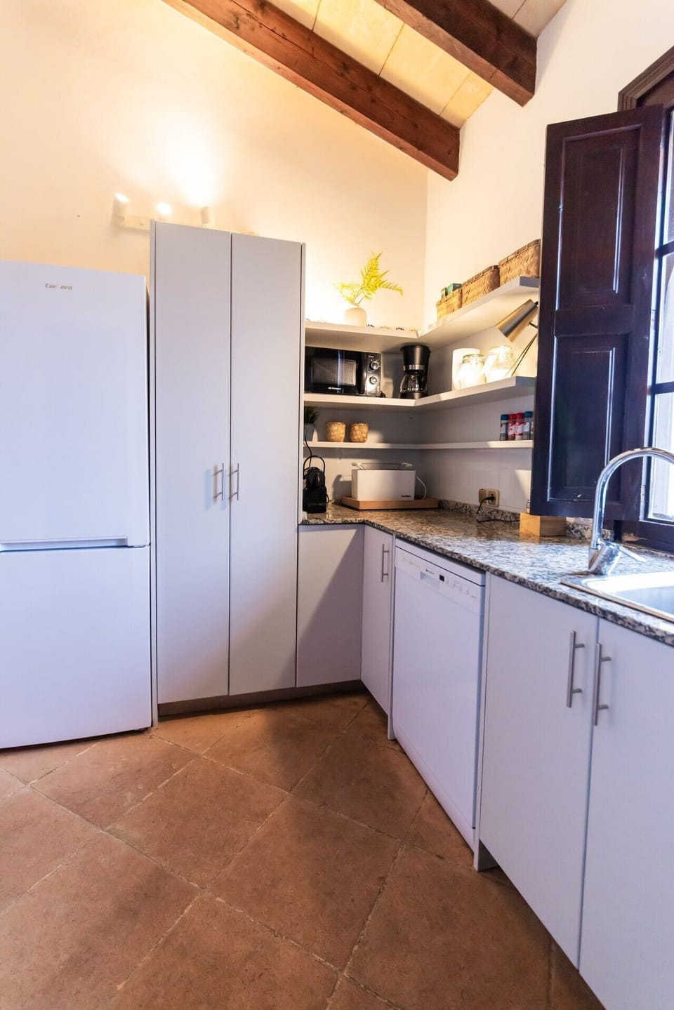 Küche OG | Tageslicht: weißer Kühlschrank + hoher Vorratsschrank + Gerätecke auf Regalen + weißer Geschirrspüler + Granit-Theke + dunkles Holzfenster mit offenem Laden
