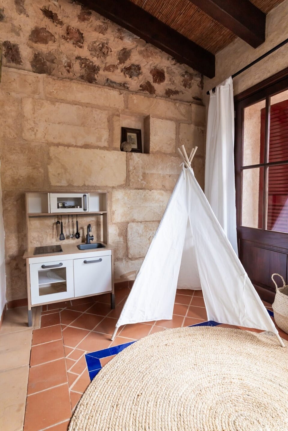 Kinderspielzimmer OG | IKEA Spielküche links + weißes Tipi-Zelt + Seegraskorb + Natursteinwand prominent, große Holz-Glastür + Juteteppich