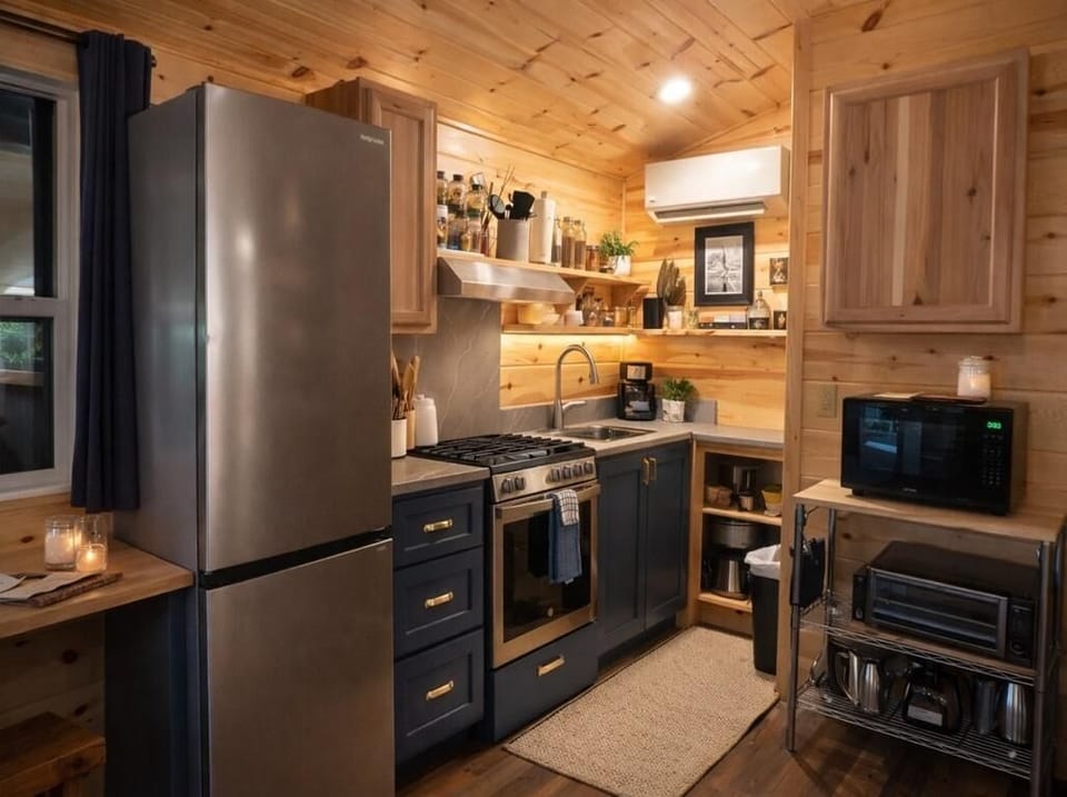 Stainless steel fridge and stove complement navy lower cabinets and natural wood walls in the kitchen.