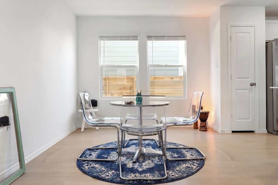 Bright kitchen and dining area featuring stainless-steel appliances, wide countertops, and a modern round table overlooking the backyard. The open layout flows into the living room, where a 55” TV creates the perfect place to relax after meals.